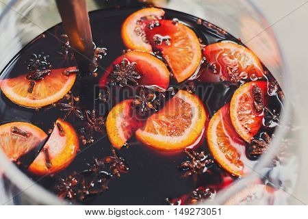 Making hot alcohol, mulled wine for sale at country fair. Glintwine from red wine with citrus and cloves in big metal stock pot, mixed with soup ladle. Closeup