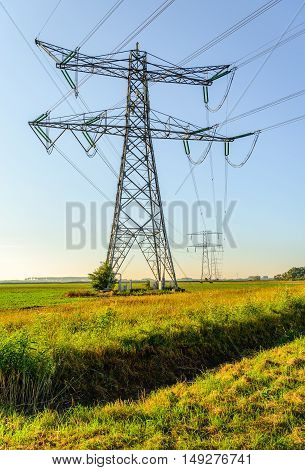 High voltage pylons and cables in a rural area in the Netherlands. It's a sunny day in the beginning of the fall season.