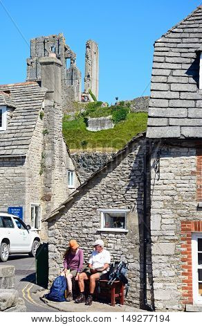CORFE, UNITED KINGDOM - JULY 19, 2016 - Couple sitting on a bench in village centre with the castle to the rear Corfe Dorset England UK Western Europe, July 19, 2016.