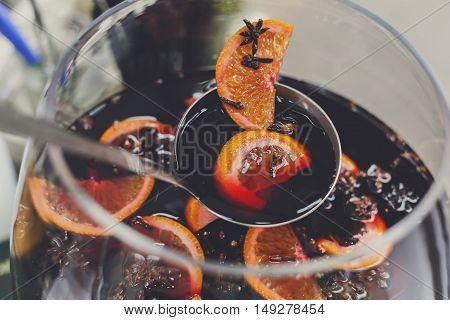 Making hot alcohol, mulled wine for sale at country fair. Glintwine from red wine with citrus and cloves in big glass, mixed with soup ladle. Closeup