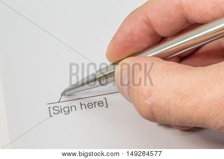 Close up of a contract with a line and the word sign here and a hand signing it with a silver pen
