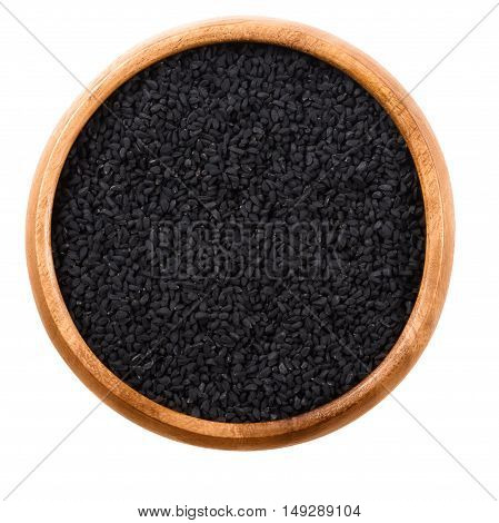 Black cumin seeds in wooden bowl over white. Dried whole fruits of Nigella sativa, also black caraway, nigella or kalonji. Used as a spice in Indian and Middle East cuisine. Isolated macro food photo.