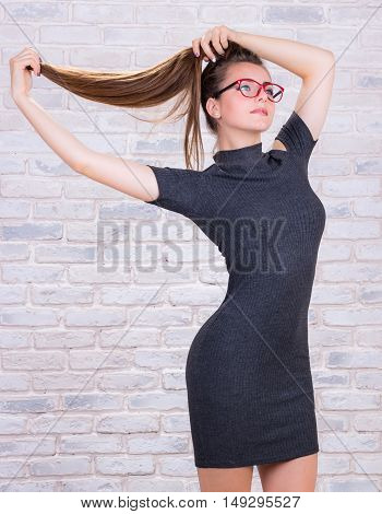 Young beautiful girl model with long hair in grey dress pulls her hair tail