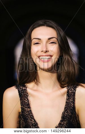 young sexy sensual woman or girl portrait with long brunette hair and pretty smiling happy face in black vest sunny day outdoor in street
