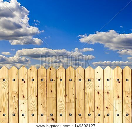 Detail of a wooden fence built with spiky wooden boards against a blue sky