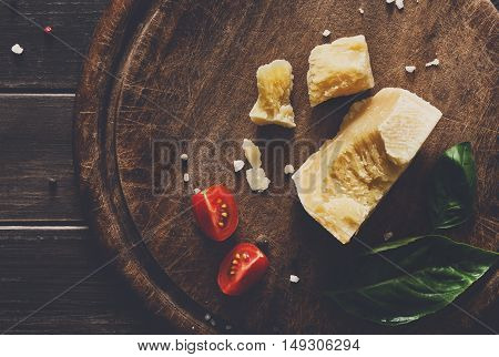 Cheese delikatessen closeup on rustic wood. Wooden desk with parmesan, camembert cuts decorated with garlic, tomato and basil, top view image