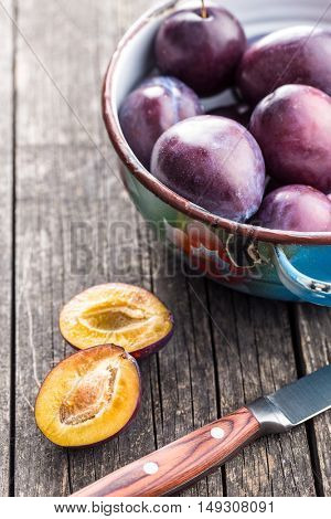 Halved ripe plums and knife on old wooden table.