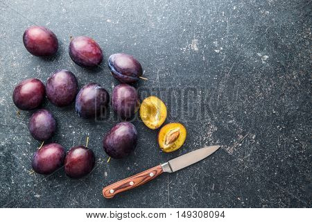 Halved ripe plums and knife on old kitchen table. Top view.