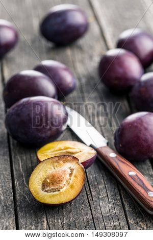 Halved ripe plums and knife on old wooden table.