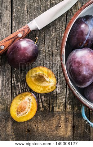 Halved ripe plums and knife on old wooden table. Top view.