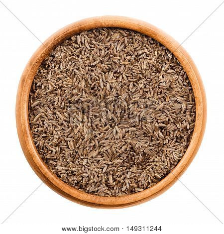 Caraway seeds in wooden bowl on white background. Dried whole fruits of Persian cumin, Carum carvi, with anise like flavor and aroma used as spice in cuisine. Isolated macro photo close up from above.