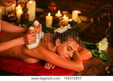 Young woman lying on wooden spa bed. Poultice hot herbal massage in spa salon. Burning candles on bachground.