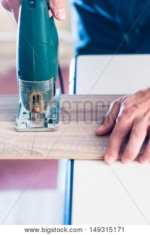 DIY worker cutting wooden panel with jig saw