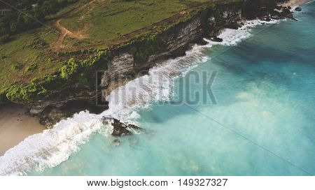 Aerial photo from flying drone of a green island with rocky cliff near Indian Ocean with swell waves an ideal place for surfing training. Beautiful nature landscape with dreamland beach and calm sea