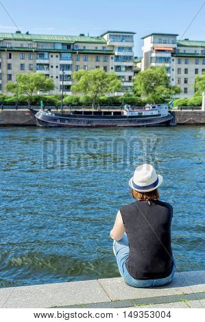 Girl in hat sitting on pier and lookingat the river
