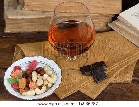 Glass of brandy and a chocolate on a old wooden table with old books