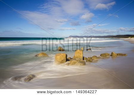 Waves in a calm sea break against the rocks on a beach called Friendly Beaches in Freycinet National Park, Tasmania