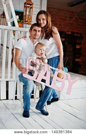 Young Caucasian Happy Family In Love Idoor Room With Letters Of The Word Baby