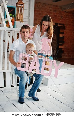 Young Caucasian Happy Family In Love Idoor Room With Letters Of The Word Baby