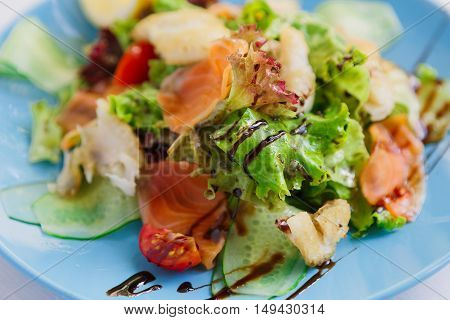 Restaurant healthy food, seafood salad closeup. Salmon and cod fish salad with vegetables and lettuce on blue plate. Appetizing dish served with sauce, dinner meal. Selective focus