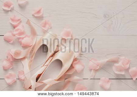 Pastel pink ballet shoes background. New pointe shoes with satin ribbon and rose petals lay on white rustic shubby chic wood, top view with copy space, soft toning