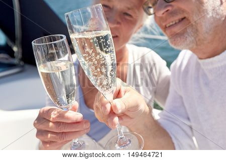sailing, age, travel, holidays and people concept - close up of happy senior couple drinking champagne on sail boat or yacht deck floating in sea