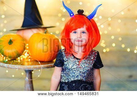 Happy deamon children during Halloween party playing around the table with pumpkins