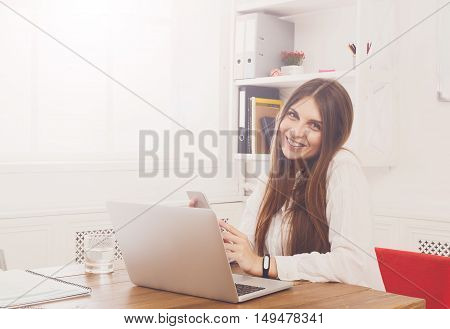 Beautiful young businesswoman sitting by wooden desk with laptop. Modern office worker in white room interior. Succesfull woman, female carreer concept.