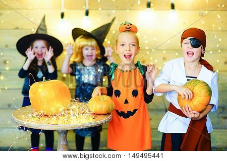 Happy group of witch children pirate and demons during Halloween party playing around the table with pumpkins