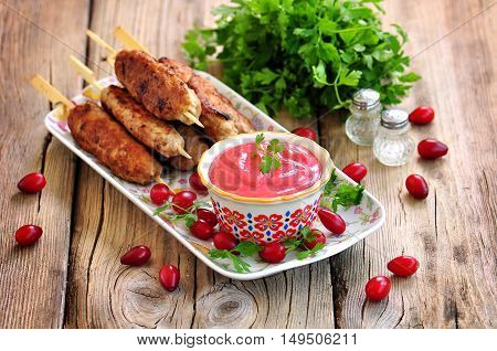 Homemade sauce dogberry with meat kebabs on wooden skewers.