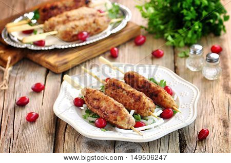 Homemade meat kebabs skewers with dogberry and onion salad on wooden background.