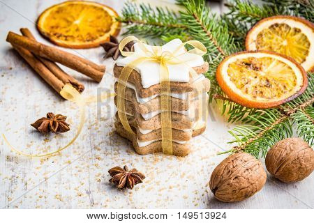 Close up of homemade butter nuts star shaped cookies with icing pine orange slicescinnamon anise walnuts and golden ribbon over white wood background. Christmas decoration.