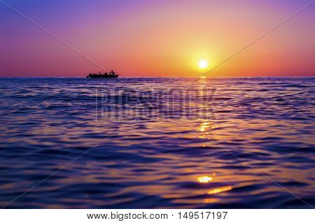Evening seascape. Silhouette of man on the row boat against the setting sun. The sun reflected off the waves. Purple pink and yellow colors. Georgia
