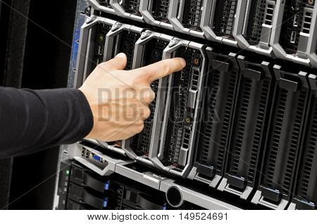 Closeup of IT technicians hand touching power button on blade server at data center