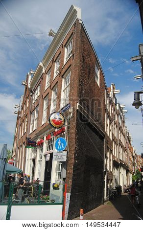 Amsterdam, The Netherlands - May 22, 2014. Street view in Amsterdam. Leaning historic building along Nieuwezijds Voorburgwal street in Amsterdam, with outdoor cafe and people.