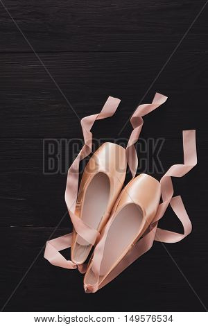 Pastel pink ballet shoes background. New pointe shoes with satin ribbon and rose petals lay on black rustic shubby chic wood, top view with copy space, vertical