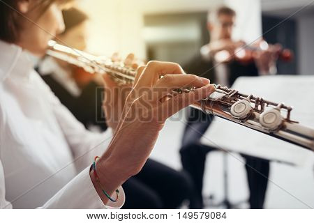 Professional female flustist playing her instrument on stage with classical music symphony orchestra