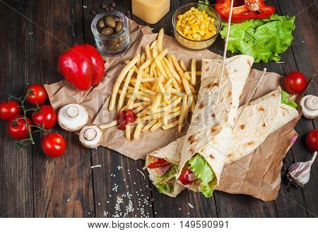 Sandwiches twisted roll Tortilla two pieces and french fries on a wooden background