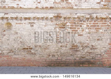 Broken old bricklaying wall from red white bricks with damaged plaster and road pavement background texture in the oldtown street