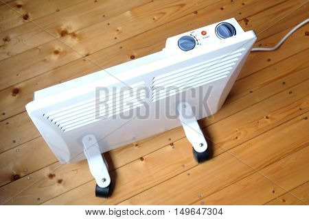 Working white electric convector heater with control panel on top on wooden floor in a house room top view closeup