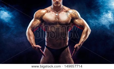 Close up on perfect abs. Strong bodybuilder with six pack.Strong bodybuilder man with perfect abs, shoulders, biceps, triceps and chest, personal fitness trainer flexing his muscles in blue, red smoke