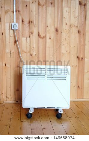 Working white electric convector heater plugged to power line in a wooaden house room front view closeup