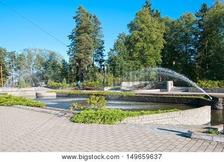 IMATRA, FINLAND - SEPTEMBER 13, 2016: Woman on the bicycle near pool with fountains not far from Spa Hotel Rantasipi Imatran Valtionhotelli in the center of the town