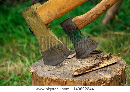 Ax in the deck on a background of green grass and firewood
