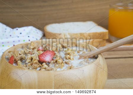 Bowl of breakfast muesli with oat and wheat flakes mixed with dried fruit and nuts in a wooden bowl for a healthy nutritious meal.Served with wholewheat bread and fresh orange juice.