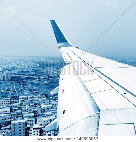 The airplane flies high above the city and the wing shines in the sun.