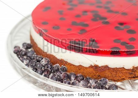 Fragment of layered cake with layers of sponge cake milk jelly and berry jelly and frozen berries on a glass cake serving dish