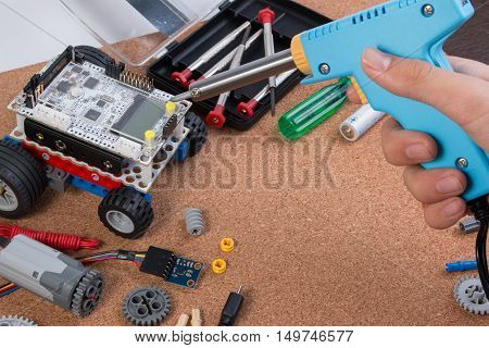 Hand Holding Soldering Iron Tool Assembling Robot With Microcontroller.
