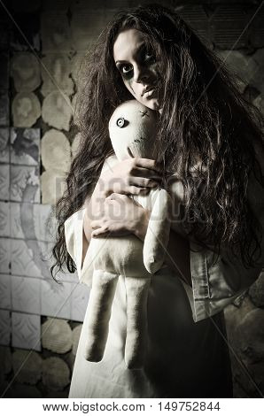 Horror style shot: a strange sad girl with moppet doll in hands