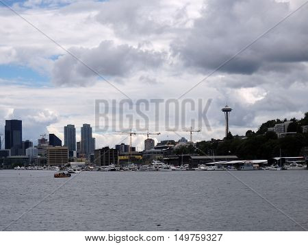 Cranes Space Needle trees and skyscrapers line in Seattle Washington USA skyline. Boats in the foreground and clouds in the sky. June 2016.